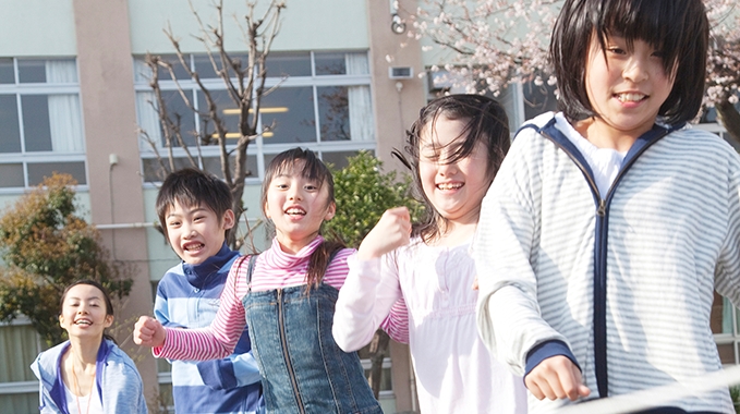 学校の校庭で遊ぶ学童に通う小学生児童と指導員